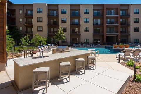 a patio with a bar and chairs in front of a swimming pool